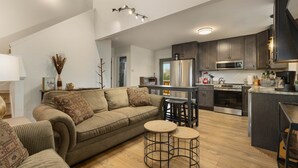 Una cocina moderna con gabinetes oscuros, electrodomésticos de acero inoxidable y una isla central. Cuenta con una zona de estar acogedora con un sofá y dos taburetes.