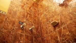 Un baño con azulejos de mármol marrón, un cabezal de ducha y un letrero que indica agua caliente.