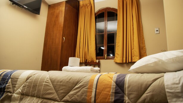 Habitación de hotel con cama, ventana con cortinas, televisión de pantalla plana montada en la pared y armario de madera.