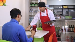 Interior de un restaurante con una mesa, sillas y un camarero sosteniendo una bandeja.