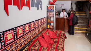 Un área de recepción con mostrador y una cama con ropa de cama estampada, además de una escalera que sube a un nivel superior.