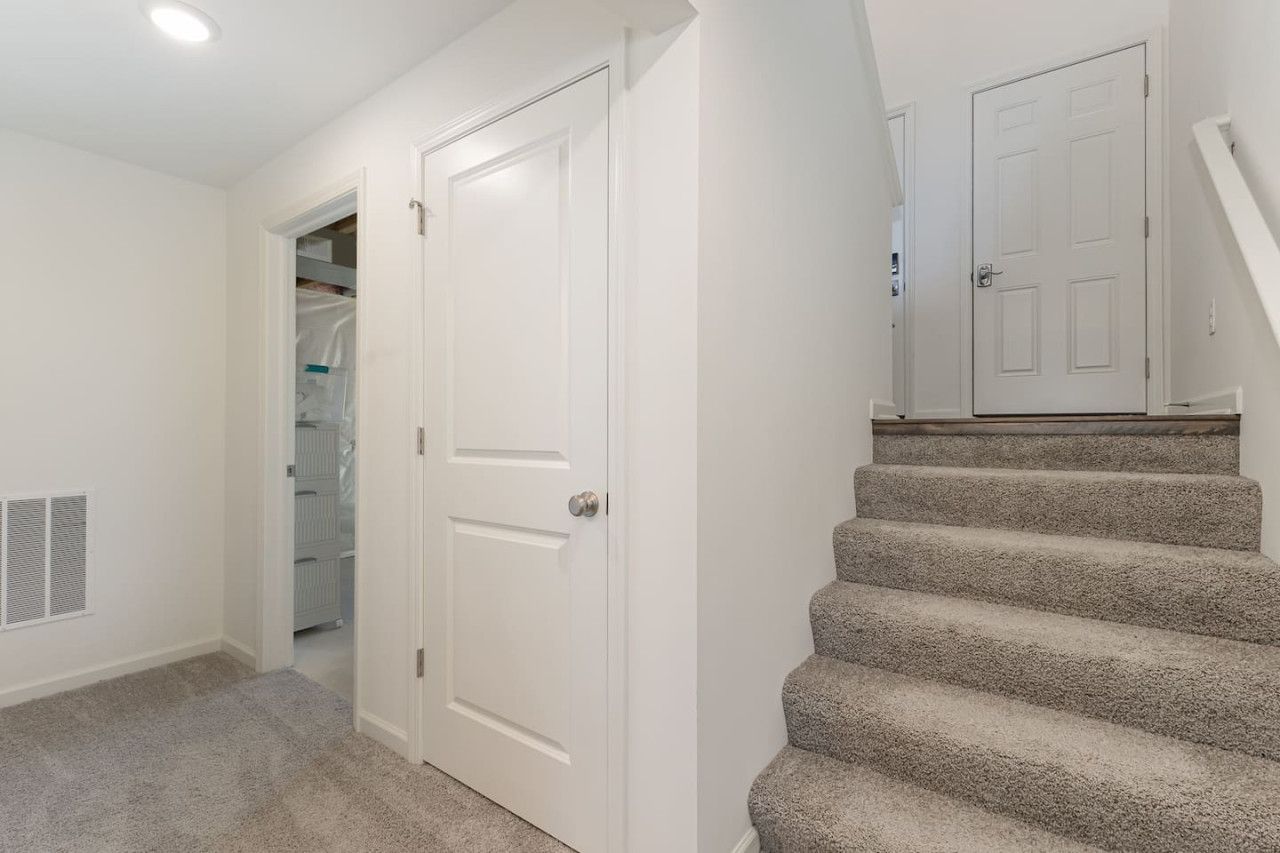 A hallway with a carpeted floor, a white door, and a staircase leading to another room.