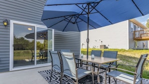 An outdoor patio with a table and chairs, a large umbrella, and a patterned rug. - Brand New House with Hot Tub! Gameroom! Workspace! (Michigan City)