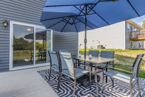 Une terrasse extérieure avec une table et des chaises, un grand parasol et un tapis à motifs.