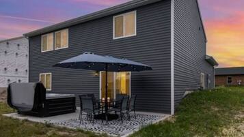 A modern two-story house with a patio area featuring a grill, outdoor seating, and a large umbrella.