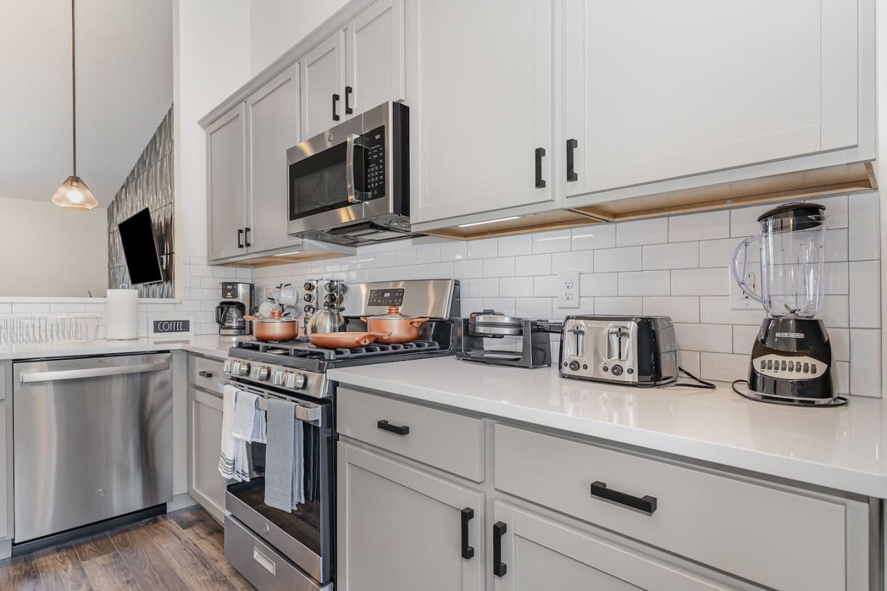 A modern kitchen with white cabinets, stainless steel appliances, a coffee station, and a blender.