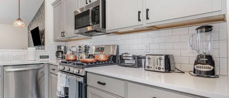 A modern kitchen with white cabinets, stainless steel appliances, a coffee station, and a blender.