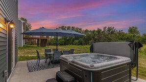 Un bain à remous sur une terrasse, avec une table et des chaises, un parasol, et une terrasse en bois en arrière-plan.