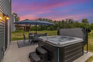 Un bain à remous sur une terrasse, avec une table et des chaises, un parasol, et une terrasse en bois en arrière-plan.