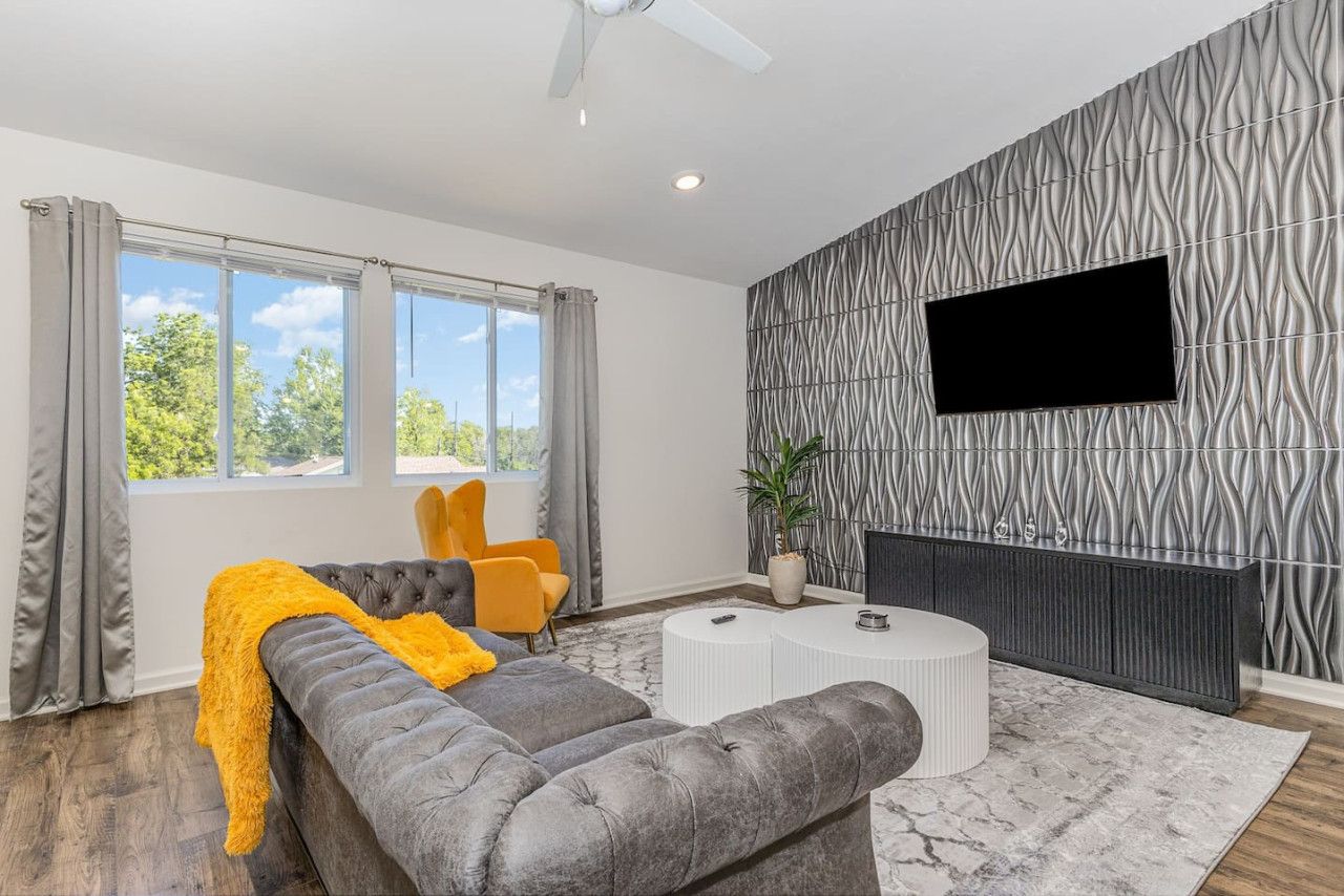 A modern living room with a grey sofa, yellow chairs, a white coffee table, and a large TV on a textured wall.