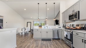 A modern kitchen with white cabinetry, stainless steel appliances, and pendant lighting. - Brand New House with Hot Tub! Gameroom! Workspace! (Michigan City)