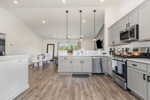 Une cuisine moderne avec des meubles blancs, des appareils en acier inoxydable et des luminaires suspendus.