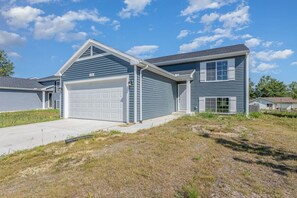 Une maison à deux étages avec un garage, une pelouse devant et un ciel dégagé.
