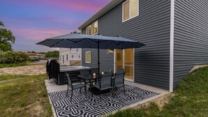 Une terrasse avec un barbecue, une table, des chaises et un parasol.