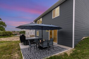 Une terrasse avec un barbecue, une table, des chaises et un parasol.