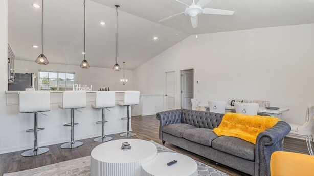 A spacious living area with a grey sofa, white bar stools, and a ceiling fan. - Brand New House with Hot Tub! Gameroom! Workspace! (Michigan City)