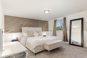 Une chambre à coucher avec un grand lit, une table de chevet, un miroir et une fenêtre avec des rideaux.