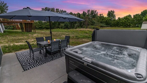 Un espace extérieur avec un jacuzzi, une table et des chaises, un parasol et une terrasse en bois en arrière-plan.