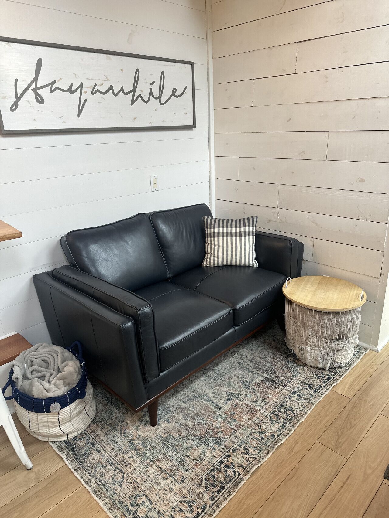 A black leather sofa with a striped pillow, a woven basket, and a rug on a wooden floor.