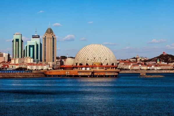 A city skyline with modern buildings and a large dome structure by the waterfront. - Tujia Sweetome Vacation Rentals (Middle Xianggang Road Lijing Yuzhu) (Qingdao)