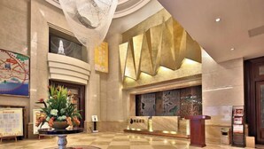 A spacious lobby with a checkered floor, a central floral arrangement, a reception desk, and a large wall with geometric patterns. - Tujia Sweetome Vacation Rentals (Middle Xianggang Road Lijing Yuzhu) (Qingdao)