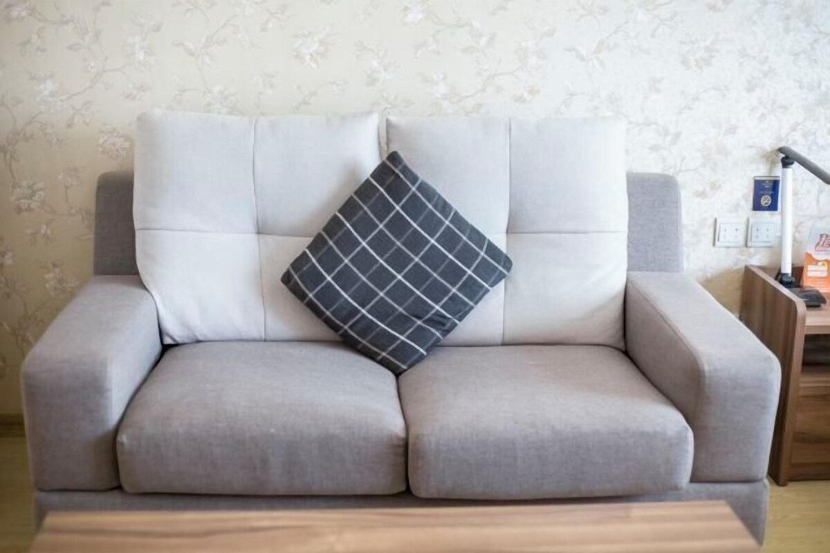 A grey sofa with a black and white checkered pillow, a wooden side table, and a lamp.