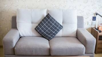 A grey sofa with a black and white checkered pillow, a wooden side table, and a lamp.
