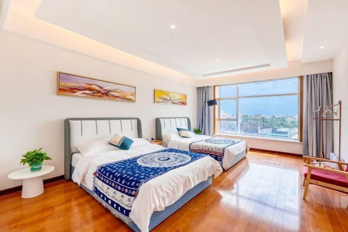 A hotel room with two beds, a large window, and artwork on the walls.