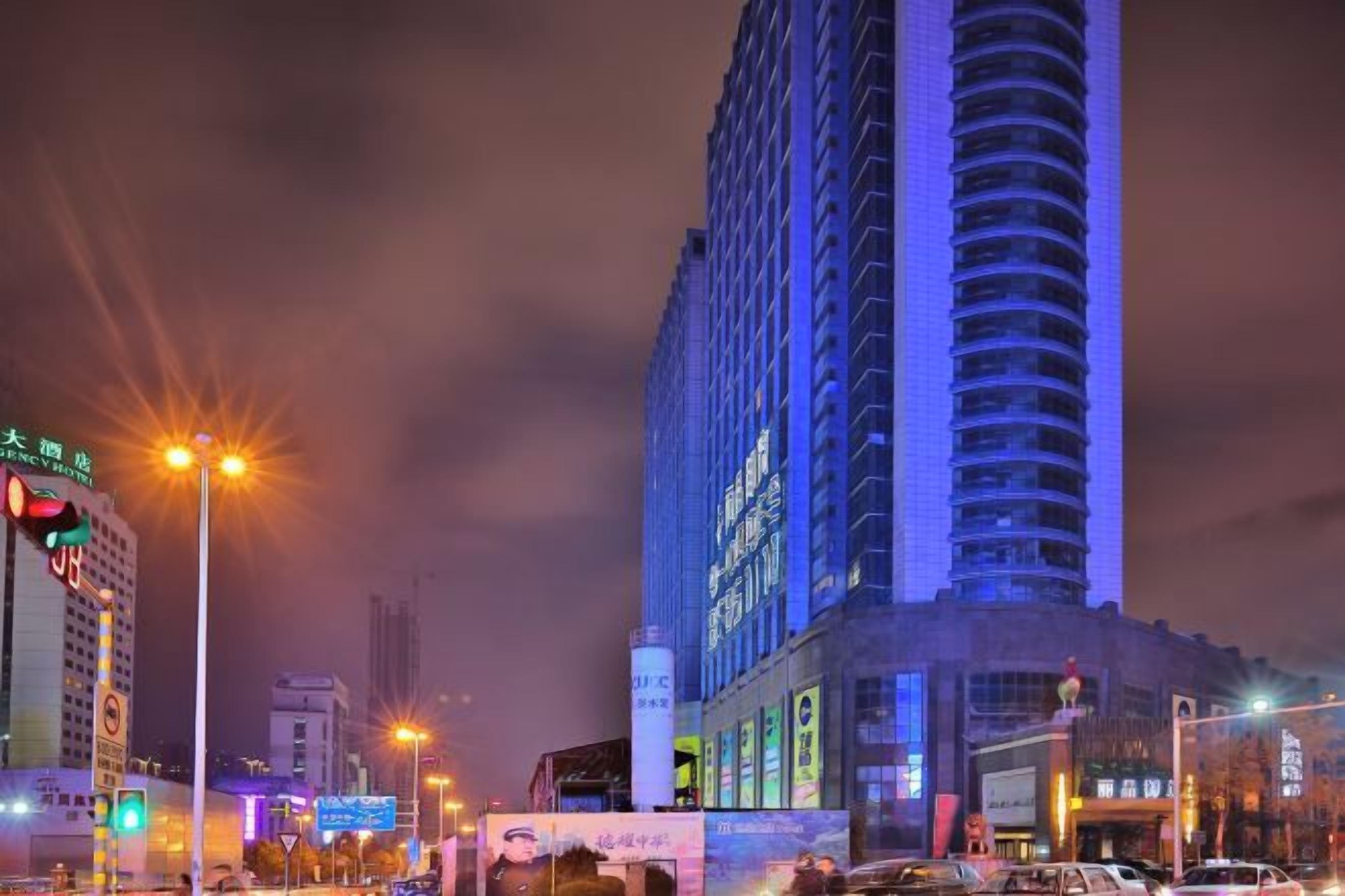 A nighttime cityscape with tall buildings, streetlights, and a busy road.