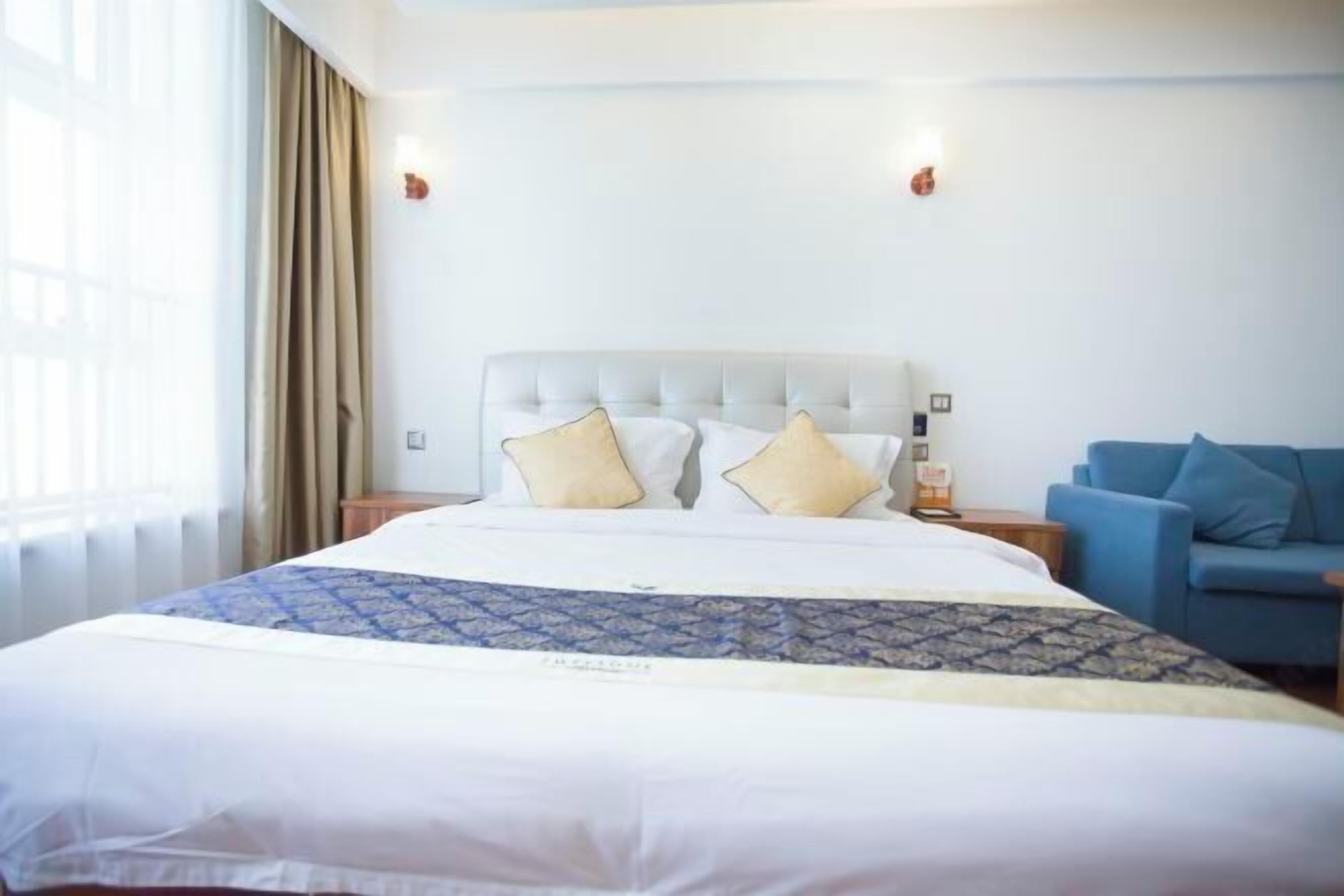 Una habitación de hotel con una cama grande, un sofá azul y una ventana con cortinas.
