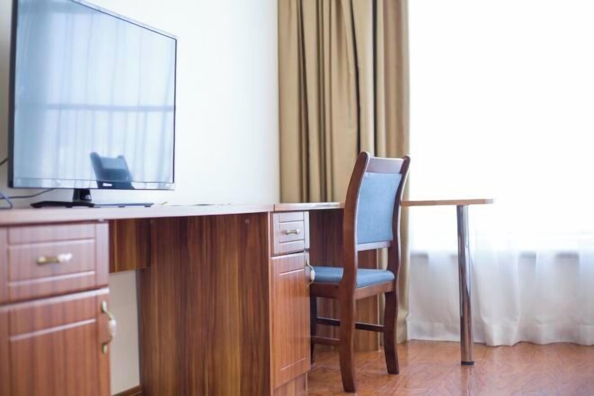 A room with a wooden desk, a chair, a television, and a window with curtains.