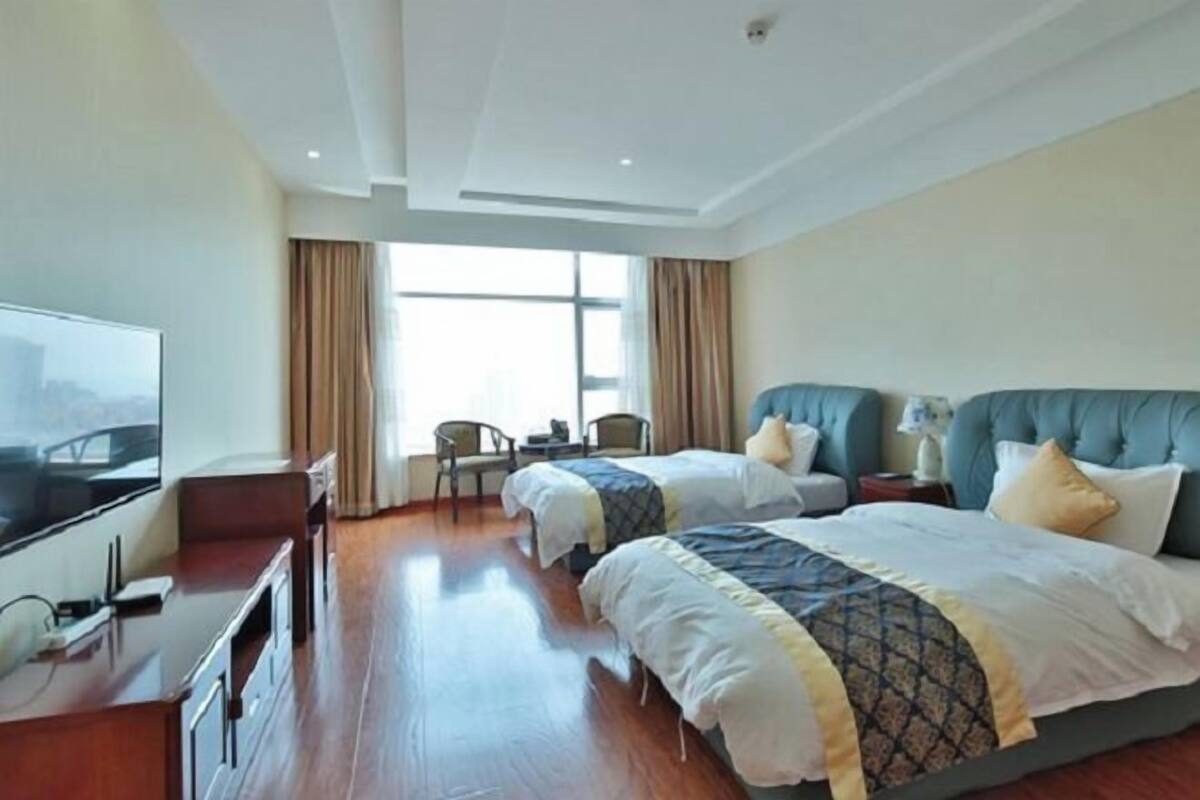 A hotel room with two beds, a TV, a desk, and a window with curtains.