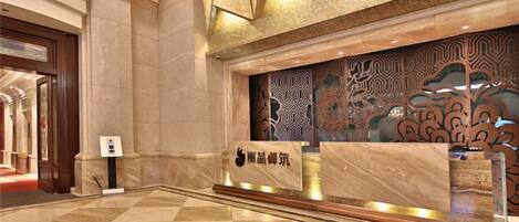 A reception area with a marble floor, a reception desk, and a decorative wall with intricate patterns.