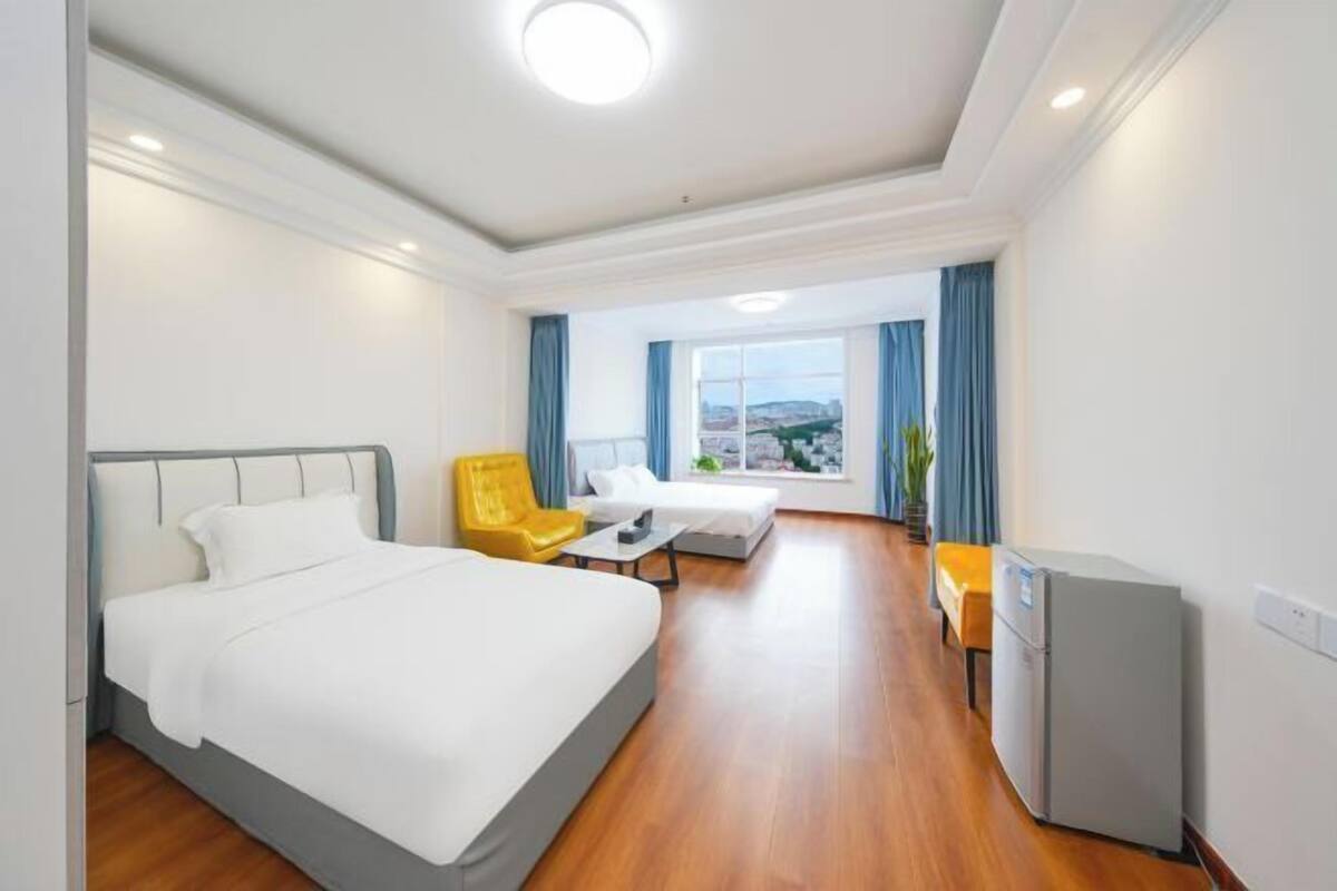 A hotel room with a bed, a desk, a chair, a small refrigerator, and a window with curtains.