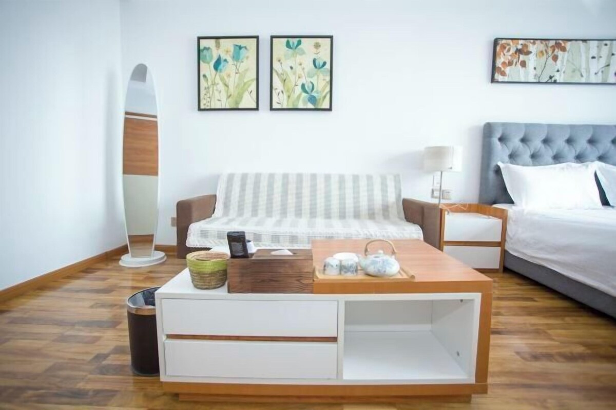 A modern bedroom with a bed, a bedside table, a lamp, a coffee table, and a wall-mounted surfboard.