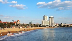 A beach with a row of buildings in the background. - Tujia Sweetome Vacation Rentals (Middle Xianggang Road Lijing Yuzhu) (Qingdao)
