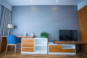A modern living room with a wooden desk, a blue chair, a television, and a plant. - Tujia Sweetome Vacation Rentals (Middle Xianggang Road Lijing Yuzhu) (Qingdao)