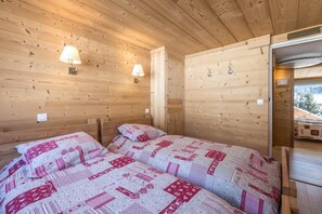 Una habitación de cabaña de madera con dos camas, cada una con colcha acolchada, y dos lámparas fijadas a la pared.