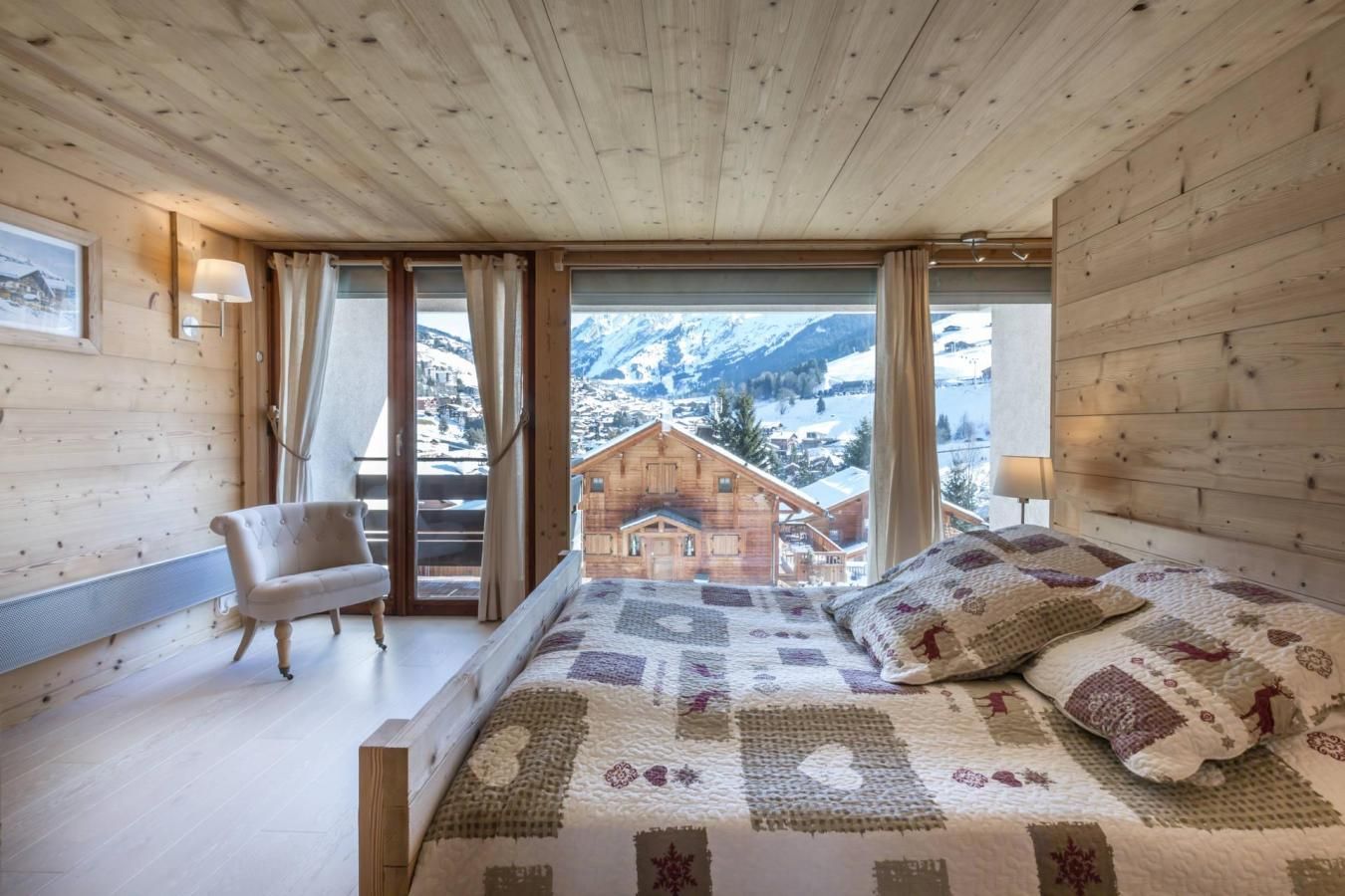 A bedroom with a large bed, a chair, and a view of a mountain village.