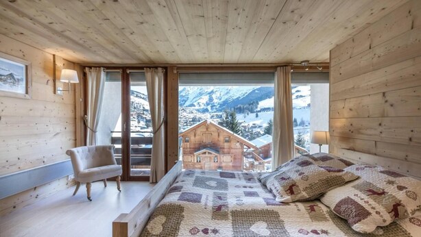 A bedroom with a large bed, a chair, and a view of a mountain village. - 70m from ski slopes, Ground floor, balcony, fireplace or stove, tv, ski locker, 74m², La Clusaz (La Clusaz)