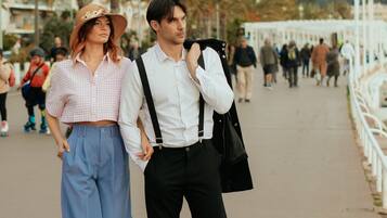 Una pareja camina por un paseo marítimo con edificios y palmeras al fondo.