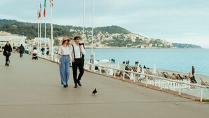 Un passeig amb vista al mar, una tanca blanca i persones passejant.