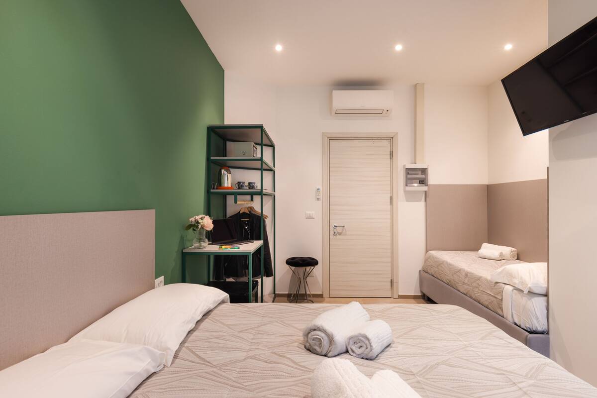 A hotel room with two beds, a desk, a wardrobe, and a television.