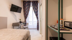 Una habitació d'hotel amb un llit, un escriptori amb un ordinador, un televisor al mur, un microones i una petita zona de cuina.