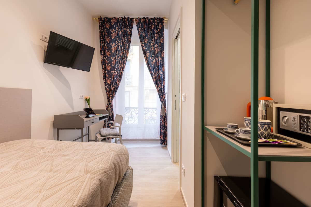 A hotel room with a bed, a desk with a computer, a TV mounted on the wall, a microwave, and a small kitchenette area.