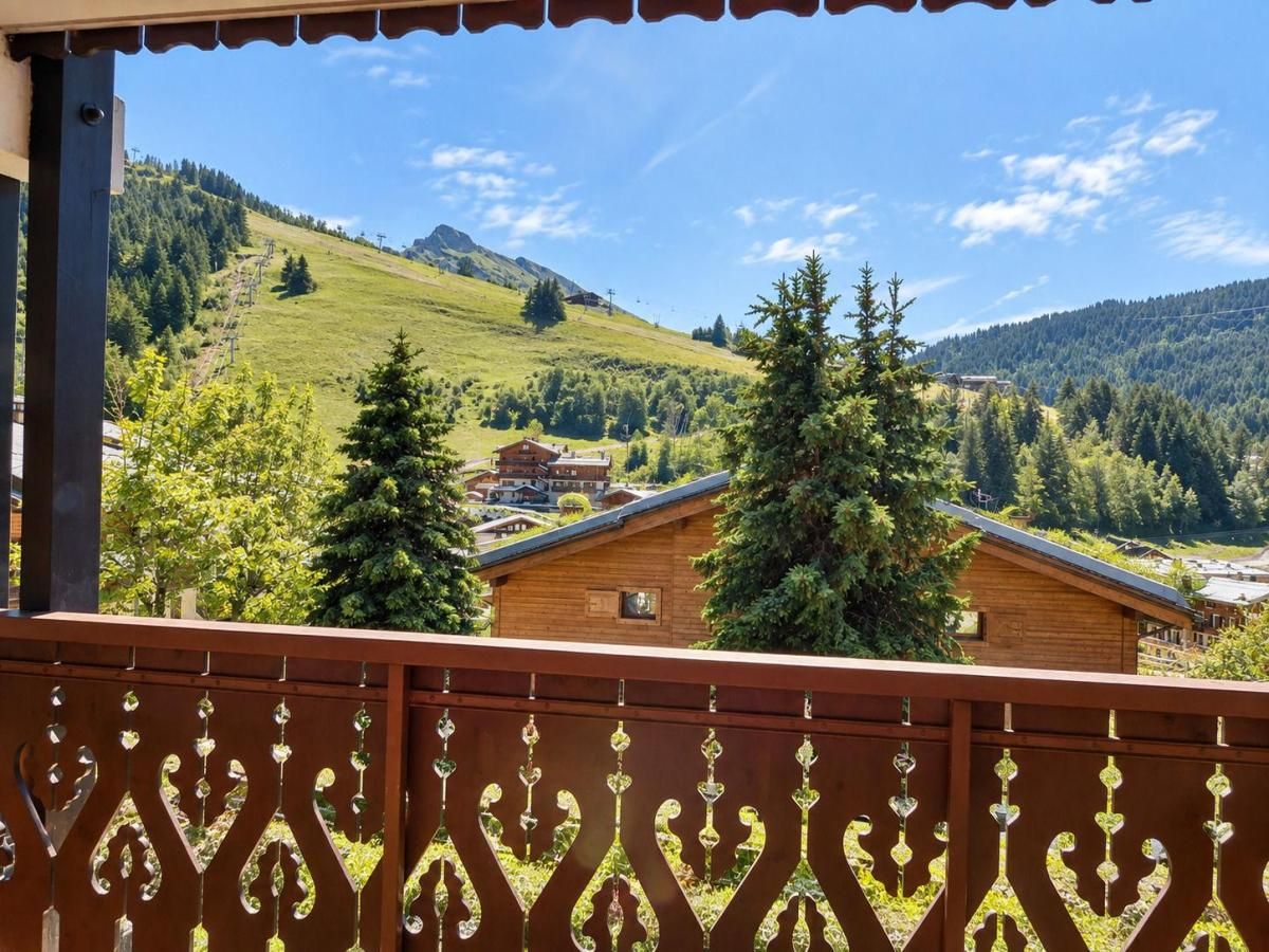 A balcony with a view of a mountain landscape, including a house and trees.