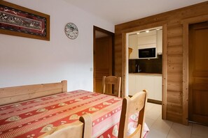A room with a bed, a table, chairs, a clock, and a kitchen area.