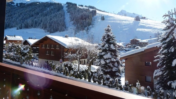 A snow-covered mountain village with wooden buildings and a ski slope in the background.