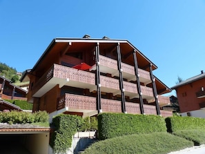 Um edifício com várias andares e varandas, cercado por vegetação.