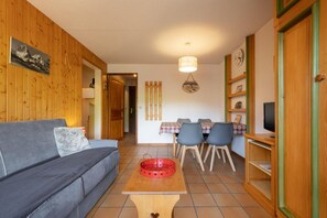 Una sala de estar acogedora con un sofá, una mesa de comedor con sillas, un televisor y paredes de madera.